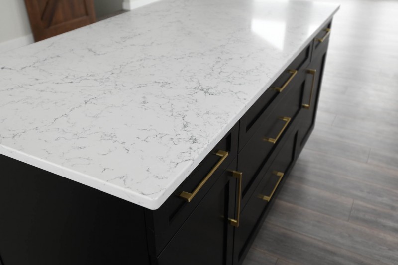 White Attica quartz counterop on black painted island cabinets with gold pulls.